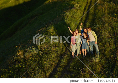 Friends waving together on hillside trail with long shadows. Friends waving together on hillside trail with long shadows. 140958014
