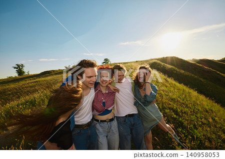 Happy friends embracing at sunset on grassy countryside hillside. 140958053