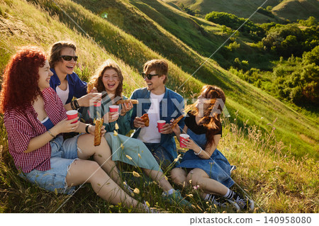 Group of young friends enjoying picnic with snacks and drinks on sunny countryside hillside. Group of young friends enjoying picnic with snacks and drinks on sunny countryside hillside. 140958080