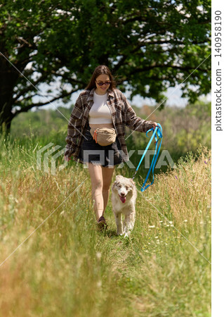Woman walking dog on leash through tall summer grass. Woman walking dog on leash through tall summer grass. 140958190