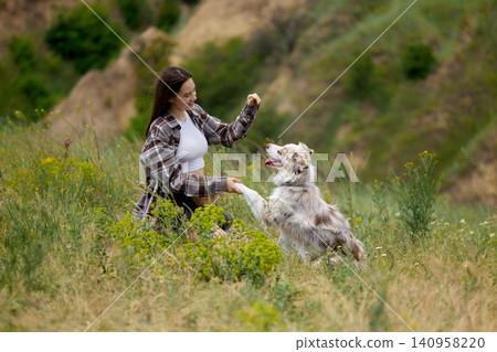 Woman teaching dog paw command with treat in countryside grass. Woman teaching dog paw command with treat in countryside grass. 140958220
