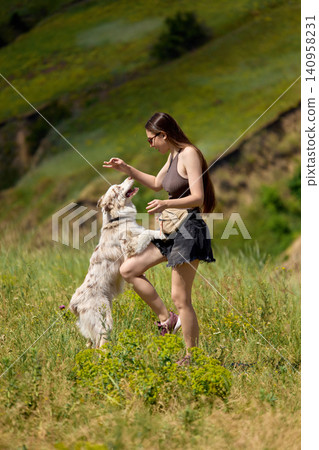 Woman training dog with treat reward in sunny countryside meadow. Woman training dog with treat reward in sunny countryside meadow. 140958231