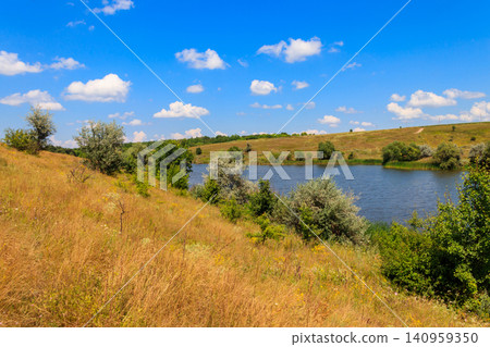 Summer landscape with beautiful lake, green meadows, hills, trees and blue sky Summer landscape with beautiful lake, green meadows, hills, trees and blue sky 140959350