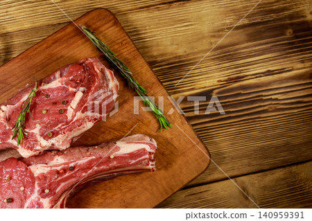 Raw fresh beef rib eye steaks on bone with spices and rosemary on wooden table. Top view Raw fresh beef rib eye steaks on bone with spices and rosemary on wooden table. Top view 140959391