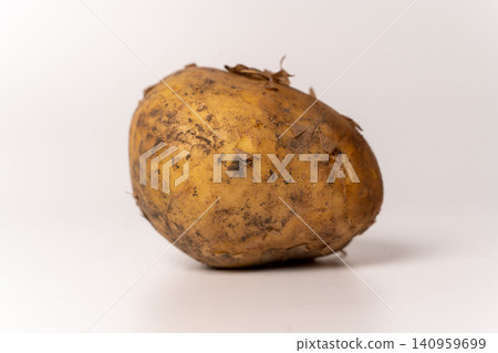 Potato sits on a plain surface with dirt on its skin in a simple setup Potato sits on a plain surface with dirt on its skin in a simple setup 140959699