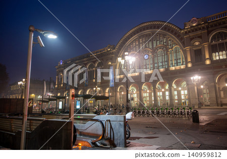 Turin, piedmont, italy. November 20, 2024. Porta nuova station in turin featuring its historic architecture illuminated at dusk with street lamps and shared bicycles 140959812