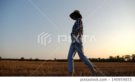 Adult agronomist in straw hat walking among barley plantation at dusk. Female farmer going through wheat meadow at sunset. Beautiful scenic landscape. Concept of agricultural business. Slow motion Adult agronomist in straw hat walking among barley plantation at dusk. Female farmer going through wheat meadow at sunset. Beautiful scenic landscape. Concept of agricultural business. Slow motion 140959855