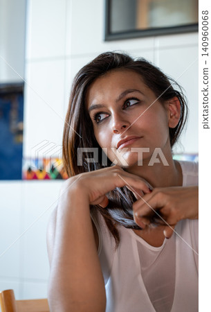 Woman with dark hair and white shirt looking away, hands resting on her chin, reflecting a moment of quiet thought and introspection in natural indoor light Woman with dark hair and white shirt looking away, hands resting on her chin, reflecting a moment of quiet thought and introspection in natural indoor light 140960068
