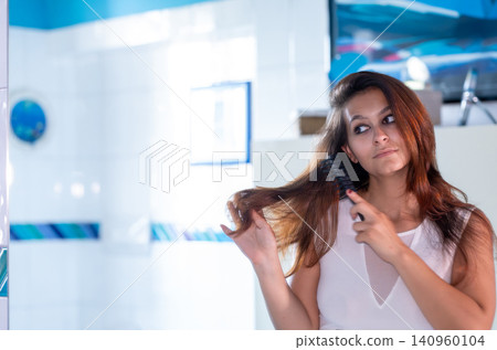 Woman brushing long brown hair, preparing for the day and taking care of herself during a morning beauty ritual inside a modern home bathroom Woman brushing long brown hair, preparing for the day and taking care of herself during a morning beauty ritual inside a modern home bathroom 140960104
