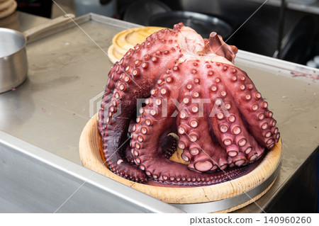 Whole cooked octopus on a wooden plate at a street food market restaurant counter ready to be sliced and served Whole cooked octopus on a wooden plate at a street food market restaurant counter ready to be sliced and served 140960260