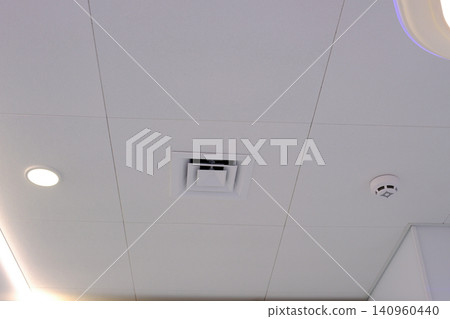 White kitchen exhaust hood mounted above stove modern ventilation system for cooking area. Smoke detector mounted on ceiling modern fire safety device in residential or commercial building White kitchen exhaust hood mounted above stove modern ventilation system for cooking area. Smoke detector mounted on ceiling modern fire safety device in residential or commercial building 140960440