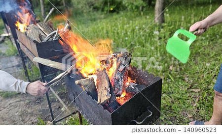 People lighting firewood in outdoor barbecue grill preparing campfire and cooking area in countryside. traditional countryside gatherings. People lighting firewood in outdoor barbecue grill preparing campfire and cooking area in countryside. traditional countryside gatherings. 140960523