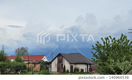Modern rural houses beneath bright blue sky with beautiful clouds in peaceful countryside setting Modern rural houses beneath bright blue sky with beautiful clouds in peaceful countryside setting 140960536