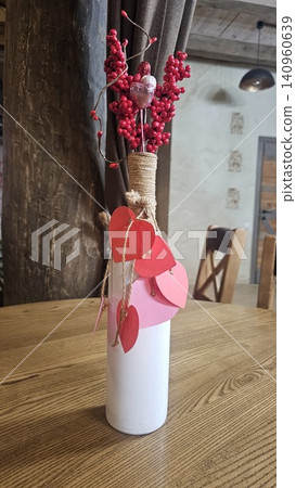 White vase with red paper hearts and decorative artificial berries on wooden table, romantic home decoration with cozy festive atmosphere White vase with red paper hearts and decorative artificial berries on wooden table, romantic home decoration with cozy festive atmosphere 140960639