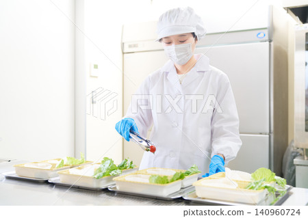 A woman working on plating at a school lunch center. A woman working on plating at a school lunch center. 140960724