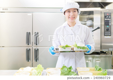 一位身穿白大褂的年輕女子正在便當工廠組裝便當盒。 140960729