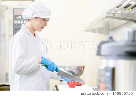 一名身穿白大褂、頭戴衛生帽的女子正在用刀切西紅柿。 一名身穿白大褂、頭戴衛生帽的女子正在用刀切西紅柿。 140960730