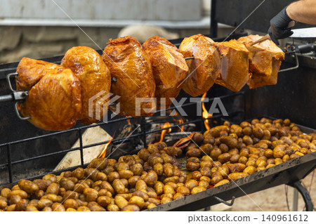 Roasting pork hocks and potatoes on a rotisserie at a street event Roasting pork hocks and potatoes on a rotisserie at a street event 140961612