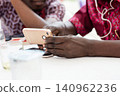 Closeup of a hand holding a mobile phone with a person in the background. 140962236