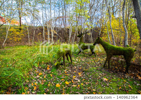 Moss-covered deer sculptures in a forested area surrounded by autumn foliage and colorful leaves on the ground Moss-covered deer sculptures in a forested area surrounded by autumn foliage and colorful leaves on the ground 140962364