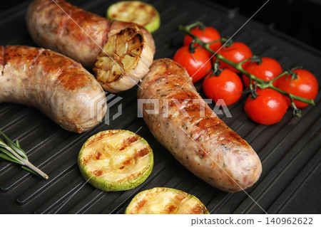 Cooking delicious fresh sausages with vegetables on modern grill Cooking delicious fresh sausages with vegetables on modern grill 140962622