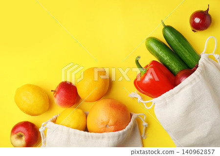 Cotton eco bags with fruits and vegetables on yellow background, flat lay. Space for text 140962857