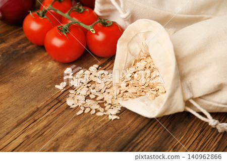 Cotton eco bags with vegetables and oat flakes on wooden table, closeup 140962866