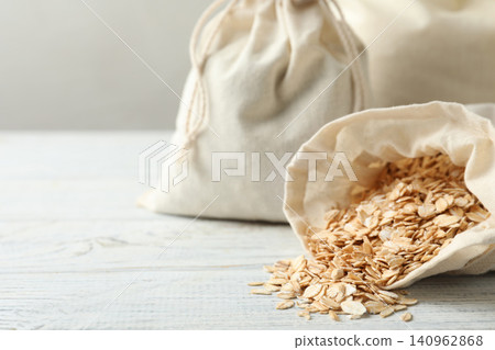 Cotton eco bags with oat flakes on white wooden table, closeup. Space for text Cotton eco bags with oat flakes on white wooden table, closeup. Space for text 140962868