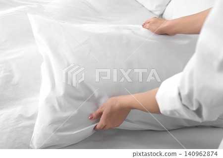 Woman fluffing soft pillow in bedroom, closeup Woman fluffing soft pillow in bedroom, closeup 140962874
