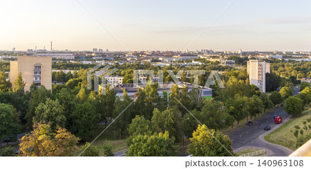 Panoramic high-angle view of a green suburban residential neighborhood with apartment buildings, dense trees, and a city skyline at sunset. Landscape Panoramic high-angle view of a green suburban residential neighborhood with apartment buildings, dense trees, and a city skyline at sunset. Landscape 140963108