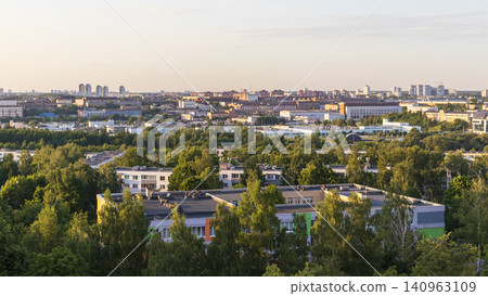 Panoramic high-angle view of a green suburban residential neighborhood with apartment buildings, dense trees, and a city skyline at sunset. Landscape Panoramic high-angle view of a green suburban residential neighborhood with apartment buildings, dense trees, and a city skyline at sunset. Landscape 140963109