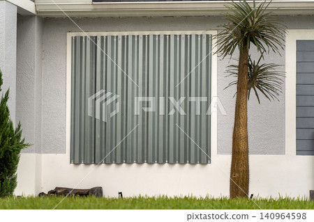 Boarded up windows with steel storm shutters for hurricane protection of residential house. Protective measures before natural disaster in Florida Boarded up windows with steel storm shutters for hurricane protection of residential house. Protective measures before natural disaster in Florida 140964598