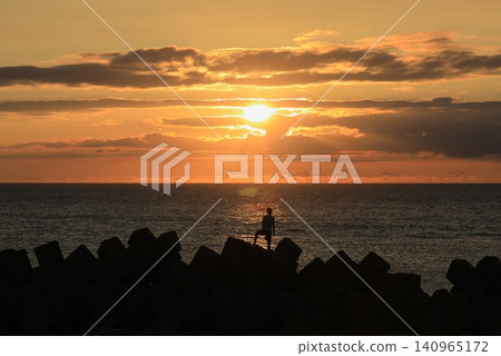 A beautiful sunset sinking into the Sea of Japan, and the silhouette of a boy standing on a tetrapod. A beautiful sunset sinking into the Sea of Japan, and the silhouette of a boy standing on a tetrapod. 140965172