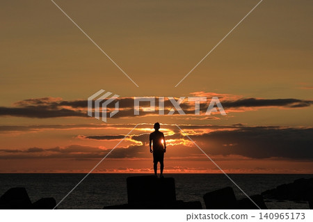 A beautiful sunset sinking into the Sea of Japan, and the silhouette of a boy standing on a tetrapod. A beautiful sunset sinking into the Sea of Japan, and the silhouette of a boy standing on a tetrapod. 140965173