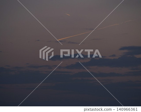 夕陽西下，餘暉染紅了天空，飛機尾跡綿延在暮色之中。 140966361