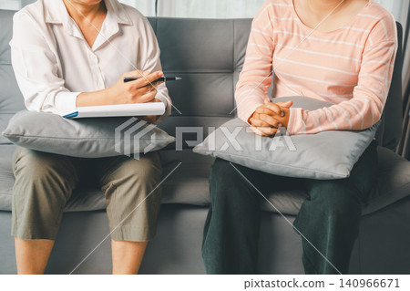 Therapist and female client sit on sofa with pillows during private counseling, showing trust, listening, mental health care, emotional support, and professional consultation indoors. Therapist and female client sit on sofa with pillows during private counseling, showing trust, listening, mental health care, emotional support, and professional consultation indoors. 140966671