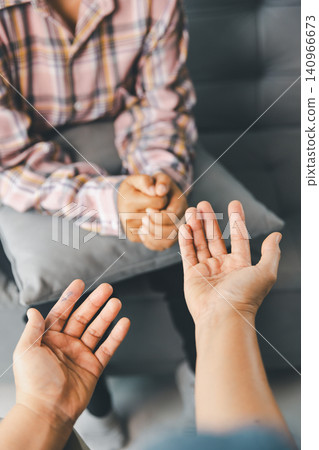 Therapist uses open hand gestures with female client during counseling on sofa, showing active listening, emotional support, mental health care, empathy, trust, guidance, and conversation indoors. Therapist uses open hand gestures with female client during counseling on sofa, showing active listening, emotional support, mental health care, empathy, trust, guidance, and conversation indoors. 140966673