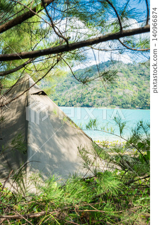 A rugged cotton tent stands in the shade of a tree, contrasting with the beautiful expanse of the tropical seascape. A rugged cotton tent stands in the shade of a tree, contrasting with the beautiful expanse of the tropical seascape. 140966874