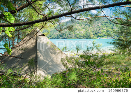 Light filtering through the pine trees and a solo campsite set up on the beach. Light filtering through the pine trees and a solo campsite set up on the beach. 140966876