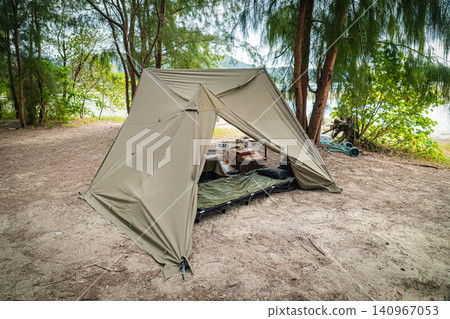 A rear view of a military-style pup tent standing proudly on a sandy area in the woods. A rear view of a military-style pup tent standing proudly on a sandy area in the woods. 140967053
