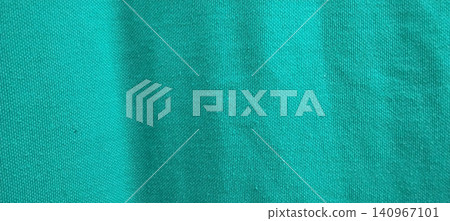 The texture of the blue-green cotton fabric features fine wrinkles and a tight knit pattern. The texture of the blue-green cotton fabric features fine wrinkles and a tight knit pattern. 140967101