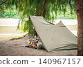 A pup tent and carefully selected gear for solo camping, set up in the shade of trees by a beautiful lake. 140967157