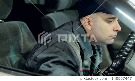 Skilled mechanic in baseball cap testing vehicle after servicing, gripping steering wheel inside automotive workshop Skilled mechanic in baseball cap testing vehicle after servicing, gripping steering wheel inside automotive workshop 140967447