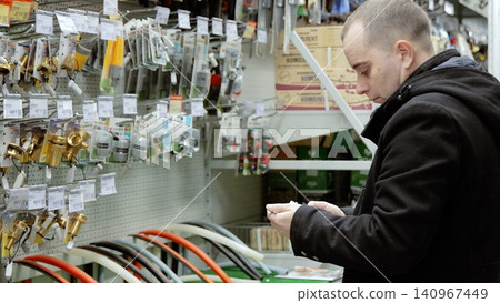 Plumber carefully choosing plumbing parts, reading label on small plastic fitting, standing in hardware store, in front of shelves with various equipment Plumber carefully choosing plumbing parts, reading label on small plastic fitting, standing in hardware store, in front of shelves with various equipment 140967449