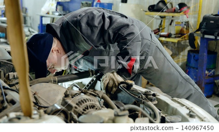 Skilled mechanic wearing protective gear carefully inspecting automotive engine inside modern workshop, focusing on precision maintenance and vehicle diagnostics Skilled mechanic wearing protective gear carefully inspecting automotive engine inside modern workshop, focusing on precision maintenance and vehicle diagnostics 140967450