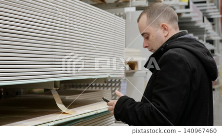 Contractor using a smartphone for selecting construction materials in a warehouse, checking quantities and prices through a mobile app while managing supplies for a project Contractor using a smartphone for selecting construction materials in a warehouse, checking quantities and prices through a mobile app while managing supplies for a project 140967460
