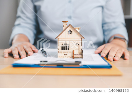 Home ownership contract concept with house model on signed documents, pen, and hands on desk, ideal for real estate sales, mortgage agreement, property insurance, and legal finance. Home ownership contract concept with house model on signed documents, pen, and hands on desk, ideal for real estate sales, mortgage agreement, property insurance, and legal finance. 140968153