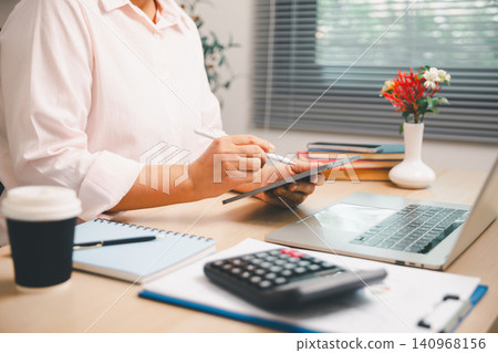 Professional working with tablet stylus beside laptop, calculator, coffee, and financial papers on office desk, ideal for digital accounting, budget analysis, productivity, and business planning. Professional working with tablet stylus beside laptop, calculator, coffee, and financial papers on office desk, ideal for digital accounting, budget analysis, productivity, and business planning. 140968156