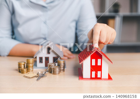 Property selection concept with finger choosing red house model among homes, coins, and keys on office desk, showing real estate comparison, mortgage budget, home buying decision, and investment Property selection concept with finger choosing red house model among homes, coins, and keys on office desk, showing real estate comparison, mortgage budget, home buying decision, and investment 140968158
