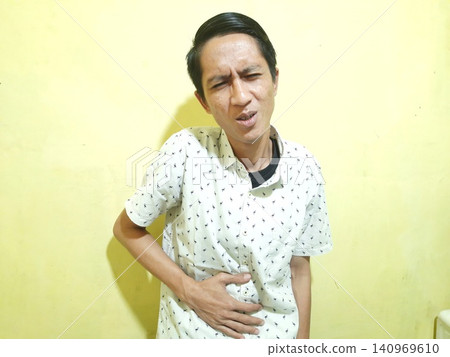 Young Asian Man Feeling Stressed with Headache Against Yellow Wall Young Asian Man Feeling Stressed with Headache Against Yellow Wall 140969610